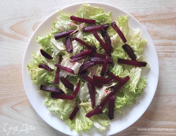 Салатные листья порвать кусочками среднего размера и выложить на блюдо, сверху — кусочки свеклы.