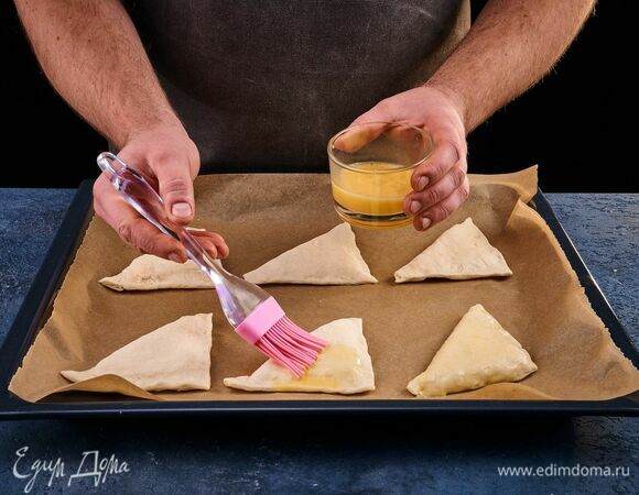 Защипните края теста. Яйцо взбейте венчиком. С помощью кулинарной кисти смажьте этой смесью заготовки.
