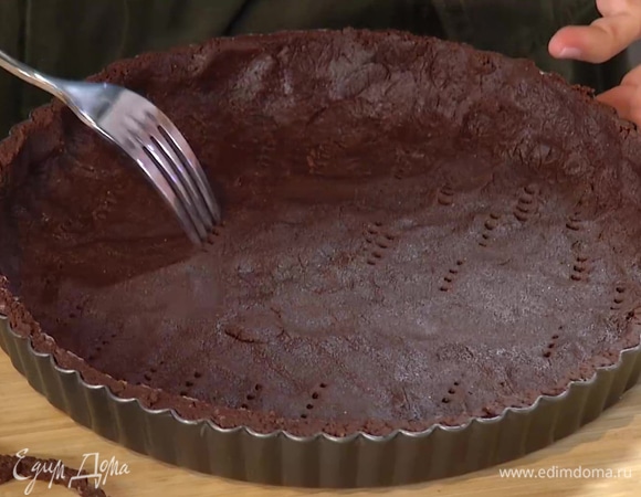 Выложить тесто в форму для выпечки тарта и равномерно распределить, лишние края обрезать ножом, затем часто наколоть тесто вилкой, накрыть пекарской бумагой, засыпать любыми бобовыми и выпекать в разогретой духовке 15–20 минут.