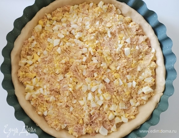 С тунца слить жидкость, немного размять вилкой и соединить с нарезанными куриными яйцами. Достать форму из холодильника и выложить начинку на тесто.