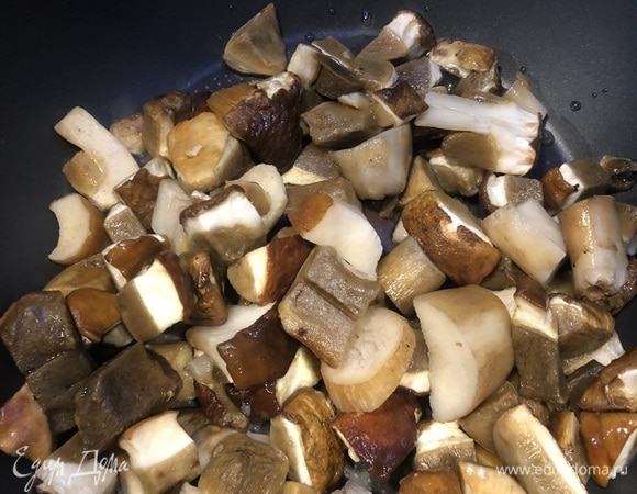 Белые грибы, не размораживая, промываем под проточной водой и сразу после этого начинаем обжаривать на оливковом масле до золотистого цвета. Для усиления вкуса можно добавить немного сухого чеснока. Ничего не солим, так как копчености, которые добавим после, и так достаточно соленые.