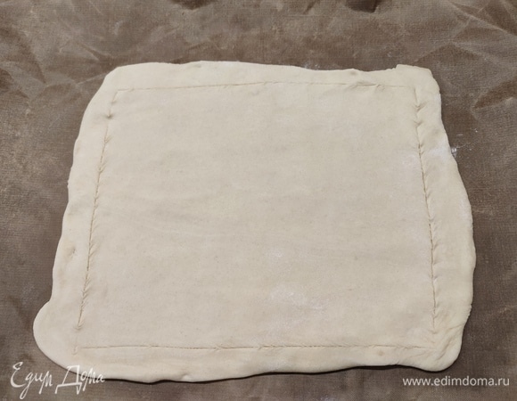 Пласт теста разморозить. Раскатать его в прямоугольник. Немного отступить от края и сделать надрезы, но не до конца, по всем сторонам. Обозначить бортики пирога.