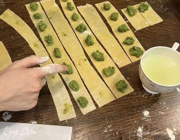 Достаем тесто. Делим его на части, каждая — с небольшой апельсин. Берем одну часть, остальное тесто снова убираем под пленку. Максимально тонко раскатываем. Идеальная толщина — 1 мм. Далее разрезаем тесто на полосы по 5 см. На каждой полоске, не надрезая, рисуем квадратики по 5 см. Должны получиться полосы с нарисованными на них квадратиками. Для чего это? Чтобы знать, куда класть начинку. На одной полосе выкладываем в центр каждого квадратика начинку, затем берем воду и смачиваем края вокруг начинки. Далее берем вторую полоску и накладываем на первую. Склеиваем все края.