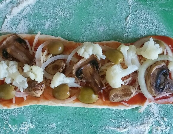 Оливки разрезать пополам. После этого на часть прямоугольников выложить грибы, цветную капусту и часть нарезанных оливок.