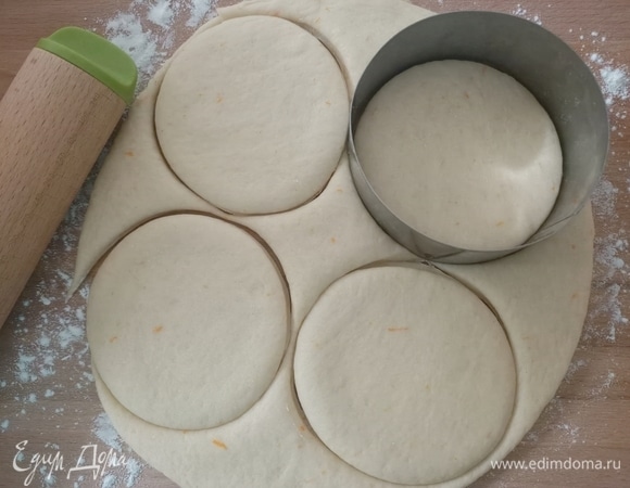 Рабочую поверхность посыпать мукой. Раскатать тесто толщиной 1 см. С помощью круглой формы вырезать заготовки для пончиков. Переложить на противень. Накрыть пищевой пленкой и поставить в теплое место еще на 1 час.