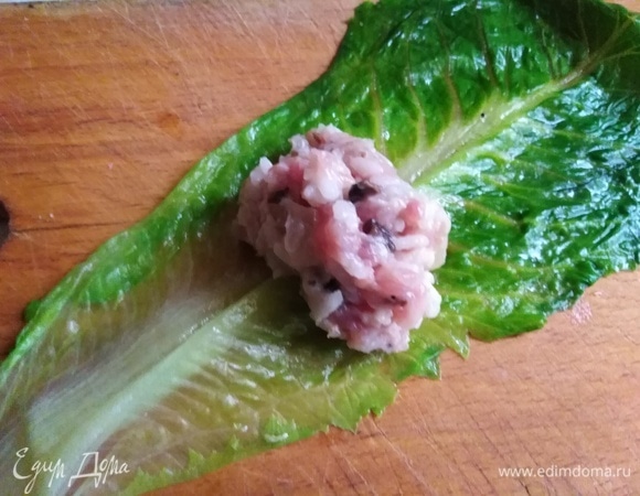 На лист салата выложить небольшую часть фарша. Свернуть рулетом, края заправить внутрь.