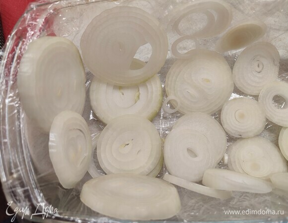 Лук нарезать кольцами. Глубокую форму застелить пищевой пленкой. Выложить большую часть лука, распределить по дну и стенкам формы.