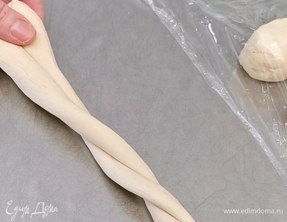 После каждый кусочек теста вытягиваем в тонкий жгут до 90 см в длину. Начинаем катать от центра, растягивая в стороны. Края должны быть толще, чем середина жгута. Затем сверните жгут пополам и скрутите веревочку. Сформируйте кольцо и тщательно укрепите концы, чтобы они не раскрылись при выпекании.