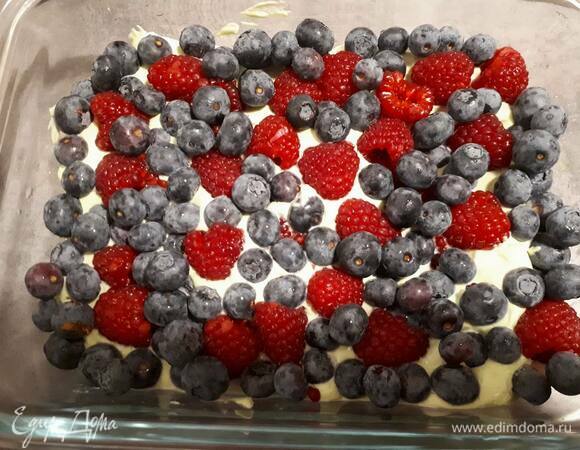 Разрежьте бисквит пополам и выложите одну половинку на дно посуды. Затем выложите половину крема и посыпьте ягодами. Накройте сверху оставшимся бисквитом и еще одним слоем крема.