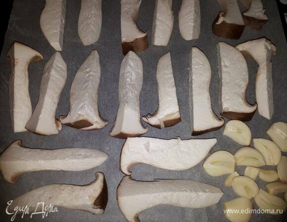 Нарежьте еригни вдоль брусочками и выложите на противень. Очистите чеснок, крупные дольки разрежьте пополам. Смажьте грибы и чеснок оливковым маслом. Запекайте в духовке в режиме «гриль» 5–7 минут при 200°C.