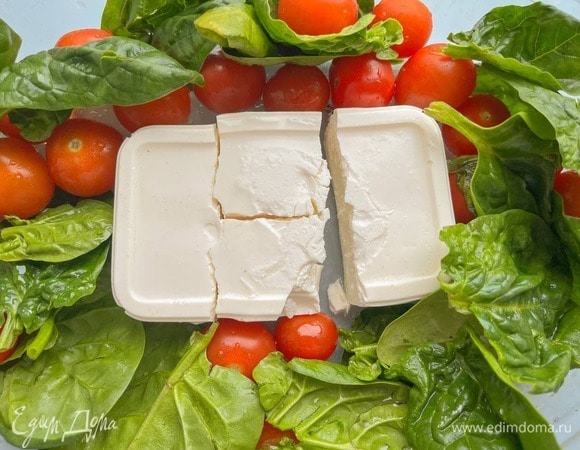 Хорошо вымойте помидоры и зелень, слейте жидкость из упаковки с сыром. Выложите в жаропрочную форму сыр, по периметру разложите помидоры и шпинат (можно добавить руколу, немного кинзы или любую другую вашу любимую зелень). Отправьте в духовку на 25–30 минут при температуре 180°C.