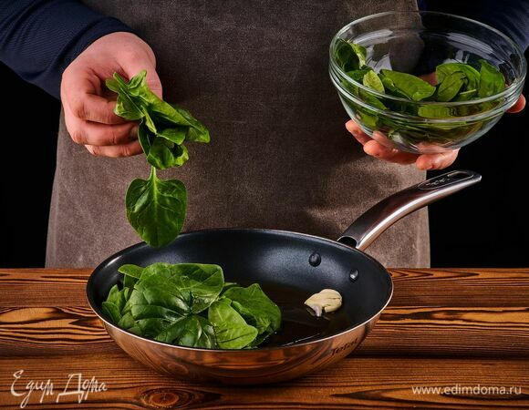 Займитесь начинкой: на сковороде растопите сливочное масло, выложите чеснок и шпинат.
