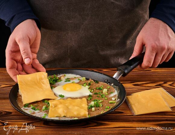 Разложите вокруг желтка ломтики сыра, чуть посолите и положите рубленый зеленый лук.<br />
С помощью лопатки заверните края блина, образуя квадрат.