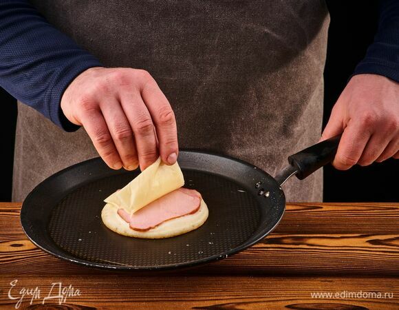 Выложите на разогретую сковороду одну ложку теста. Чуть подождите и сразу положите сверху ломтик карбонада и ломтик сыра Hochland.