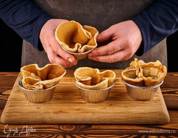 В жаропрочные формочки для кексов выложите по блину, аккуратно расправив края. Или поставьте на противень жаропрочный стакан и накройте блином. Оставьте корзинки из блинов подсушиться в разогретой до 160°С духовке примерно на 10 минут. Затем достаньте и дайте остыть.