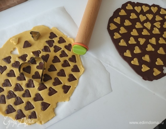 На пергаментной бумаге раскатать тесто в пласт толщиной примерно 0,5–0,7 см. С помощью маленькой формочки вырезать сердечки и поменять их местами. В светлое тесто вставить темные сердечки, а в темное — светлые.