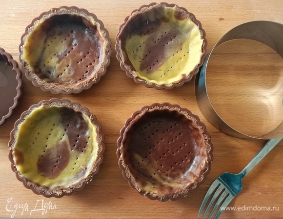 Раскатать тесто между двух листов пергамента. С помощью круглой формы диаметром 12 см вырезать кружки. Поместите тесто в силиконовые формочки. Дно наколоть вилкой. Поставить формочки с тестом в холодильник до использования.