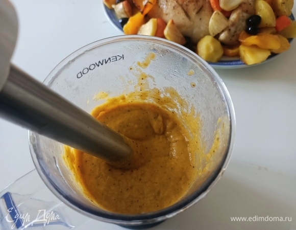 После приготовления достать курицу из духовки и положите ее на сервировочное блюдо вместе с половиной овощей в качестве гарнира. Вторую половину овощей (вместе с жидкостью от варки) используем для приготовления соуса: овощи выложить в емкость, залить бульоном и пробить блендером, пока не получится густой однородный соус, который подается на стол вместе с нашей курицей.