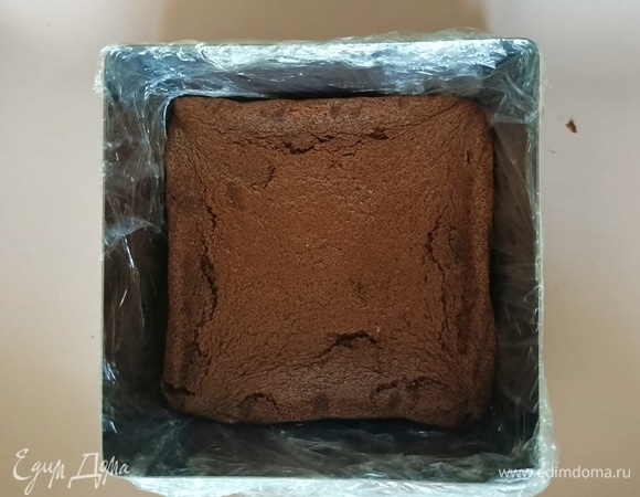 Далее берем форму размером немно мешьше, чем выпекали бисквит (у меня 10×10), оборачиваем ее пищевой пленкой. Вырезаем бисквит по фоме и укладываем его на дно формы. Остатки я использую для украшения.