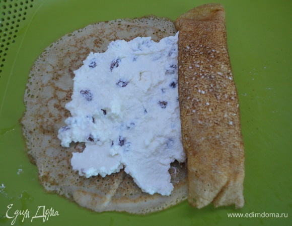 Для творожной начинки смешайте творог со сметаной, сахаром, ванильным сахаром и чистым изюмом. На два блина, лежащих внахлест, выложите начинку и заверните рулетом.