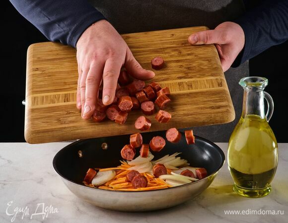 На сковороде с растительным маслом обжарьте лук и морковь. Добавьте нарезанные колбаски, потушите.