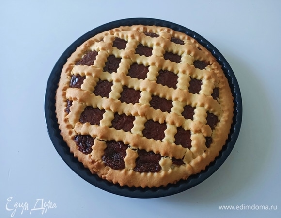 Оставшееся тесто раскатать и нарезать полосками шириной примерно 1 см. Выложить аккуратно полоски поверх начинки в виде решетки. Выпекать кростату в предварительно разогретой до 170°С духовке в течение 35–40 минут, до золотистого цвета. Готовую выпечку остудить в форме, затем аккуратно извлечь и подавать. Приятного аппетита!