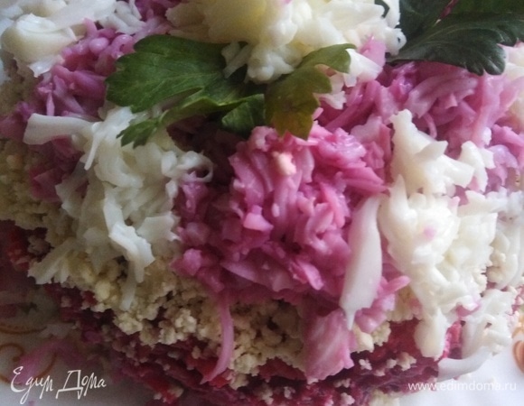 Третий слой — измельченные подсоленные желтки с тертым чесноком. Сверху покрываем тертыми на мелкой терке белками.