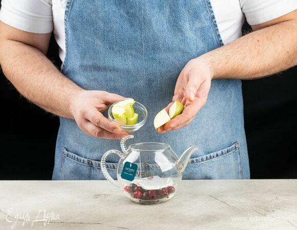 Выложите клюкву. Яблоко нарежьте дольками и тоже добавьте в чайник.