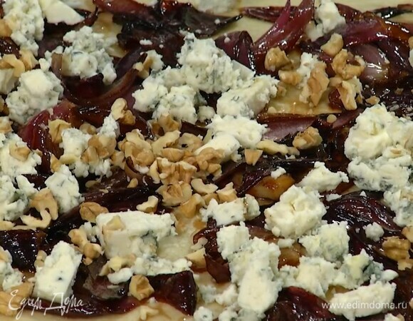 Выпекать фокаччу в разогретой духовке 10 минут, затем разложить сверху карамелизированный лук, сыр и орехи, понизить температуру в духовке до 170°С и выпекать хлеб еще 15 минут.