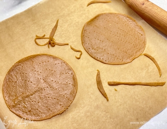 Теперь нужно раскатать заготовки, толщиной 2 мм. И вырезать из них круги диаметром 16 см (обрезки также выпечь). Удобнее раскатывать и вырезать тесто сразу на пергаменте. Проколоть корж вилкой и выпекать при 170°C около 6 минут. До румяности. Готовые коржи сразу снять с пергамента и дать остыть на ровной поверхности.