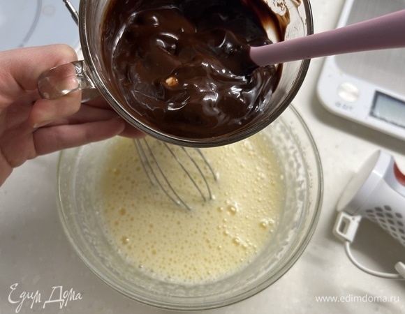 Отдельно в миске взбить яйца с сахаром в пышную белую пену. Добавить остывший шоколад с маслом и еще раз перемешать.