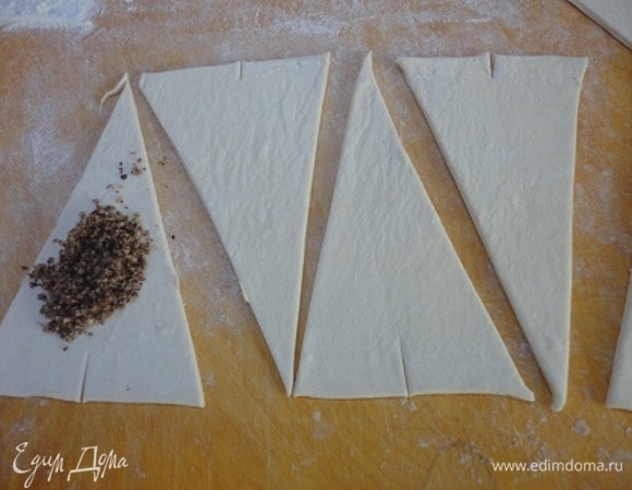 Каждый пласт раскатайте (в одном направлении) в полосу и нарежьте на треугольники. В основании каждого сделайте небольшой надрез, так круассаны будут легче заворачиваться в дугу. Выкладывайте по 1 ч. л. начинки и заворачивайте.