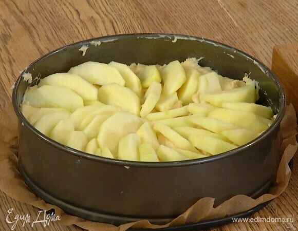 Дно разъемной формы выстелить бумагой для выпечки, выложить тесто и равномерно распределить, сверху веером разложить оставшиеся яблоки и посыпать сахаром.