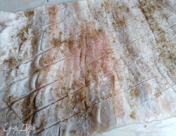 На свиной шкурке по остаточному слою сала сделать неглубокие надрезы по всей площади. Посолить, посыпать аджикой.