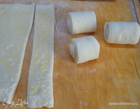 Тесто разделить на две части и каждую раскатать в прямоугольник. Смазать растопленным маслом и нарезать на полоски. У меня была цедра, и я разложила ее на часть полосок. Каждую полоску скатать в рулетик и выложить на противень. Оставить на 30 минут для подъема. Включить духовку на 180°C.