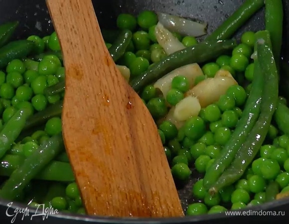 Разогреть в сковороде сливочное и оливковое масло, выложить мякоть чеснока и размять лопаткой, затем добавить размороженную фасоль и горошек.