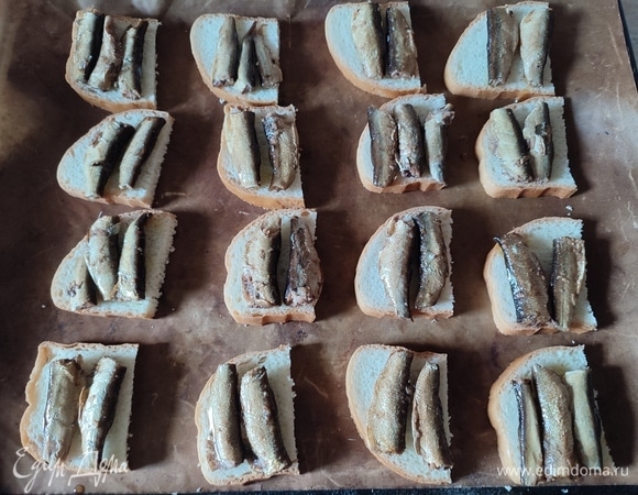 Кусочки хлеба разрезать пополам, разложить на противень, на каждую половинку выложить по две рыбки.