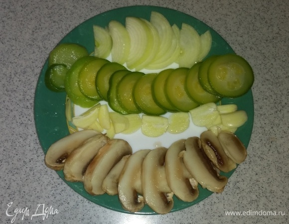 Для приготовления этого блюда я использовала замороженные кабачок и шампиньоны, можно брать и свежие (вес кабачков и шампиньонов указан после разморозки). Поэтому перед началом приготовления их нужно разморозить при комнатной температуре. Кабачок нарезать кружками, шампиньоны и зубчики чеснока нарезать пластинками, репчатый лук нужно нарезать дольками.