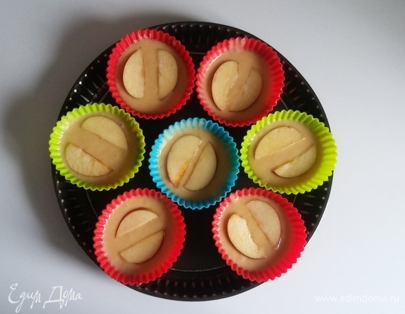 У яблока нужно удалить середину и нарезать его тонкими дольками. После чего разложить тесто по формочкам для маффинов и поверх теста выложить в каждую формочку яблочные дольки.