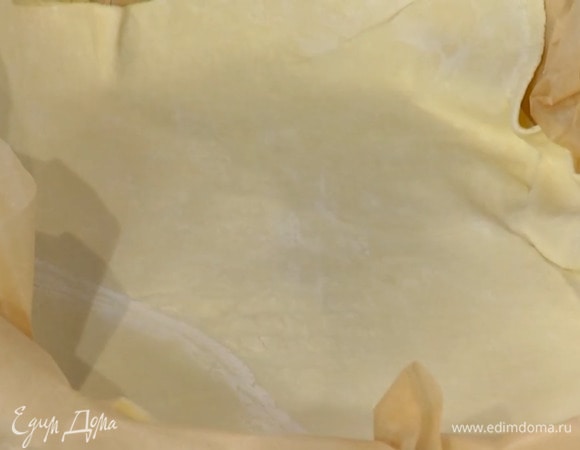 Тесто предварительно разморозить, затем раскатать на бумаге для выпечки в тонкий пласт и выложить вместе с бумагой в жаропрочную керамическую форму, так чтобы получились бортики.