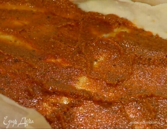 Часто наколоть тесто вилкой и, немного отступив от краев, смазать его соусом песто, а затем хариссой.