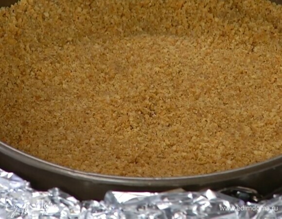 Дно двух разъемных форм разного размера выстелить бумагой для выпечки и обернуть их снаружи пищевой фольгой, затем разложить в них печенье с маслом и плотно утрамбовать, так чтобы получились коржи.