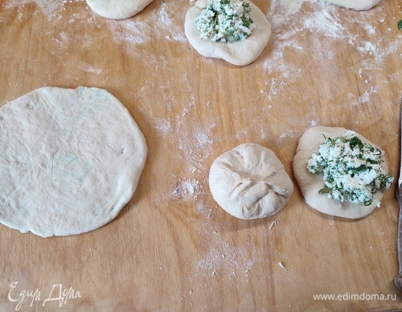 Каждый колобок немного раскатать в лепешку. На середину положить начинку, чуть больше столовой ложки. Стянуть края лепешки кверху и хорошо защипать. Раскатать в тонкую лепешку.