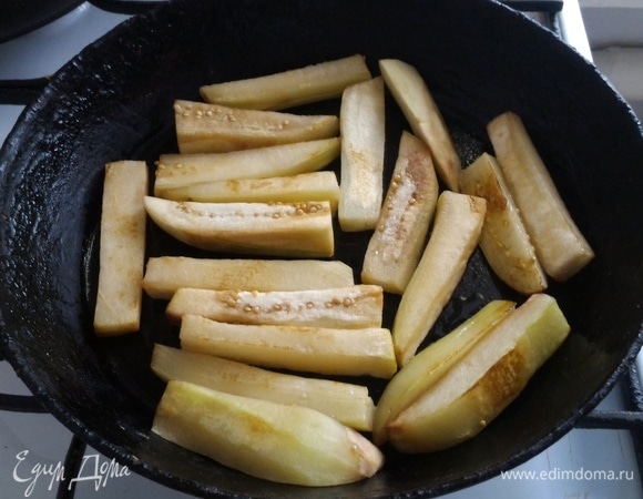 В сковороде разогрейте часть растительного масла для жарки. Порциями обжарьте бруски баклажанов до румяного цвета. Затем выложите баклажаны на тарелку. Обжарьте остальную часть, используя то же растительное масло. 