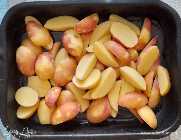 Очищенный картофель снова вымойте и обсушите бумажным полотенцем. Крупные клубни разрежьте вдоль на четыре части, мелкие — на две. Выложите картофель в форму для запекания.