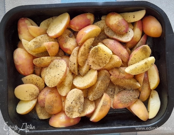 Полейте картофель растительным маслом, посыпьте хмели-сунели и черным молотым перцем, перемешайте. Дайте постоять 10 минут. Затем поставьте форму с картофелем в духовку, разогретую до 200°C.