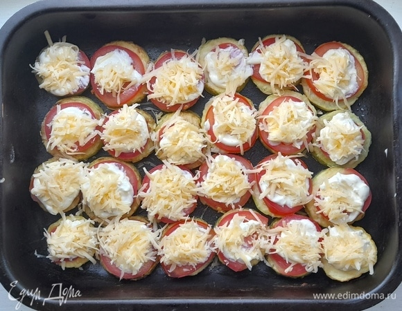 Посыпать сыром помидоры со сметаной. Поставить форму с кабачками и помидорами в духовку, разогретую до 180°C, и запекать 12–15 минут.