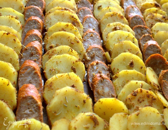 На противень постелите пергамент и разложите картофель с колбасой, чередуя кружочки.