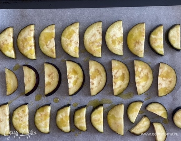 Баклажан помыть и нарезать полукружьями. Выложить на противень на лист пергамента, сбрызнуть оливковым маслом и запечь в предварительно разогретой до 200°C духовке в течение 15–20 минут.