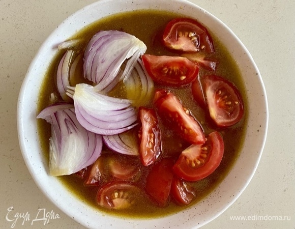 Нарезать остальные овощи: помидоры — небольшими ломтиками, красный лук — клиньями. Поместить их в соус и оставить на время, пока запекаются баклажаны.